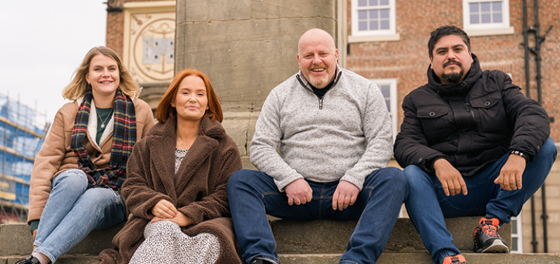 2 women and 2 men sat outside on some steps in front of a statue