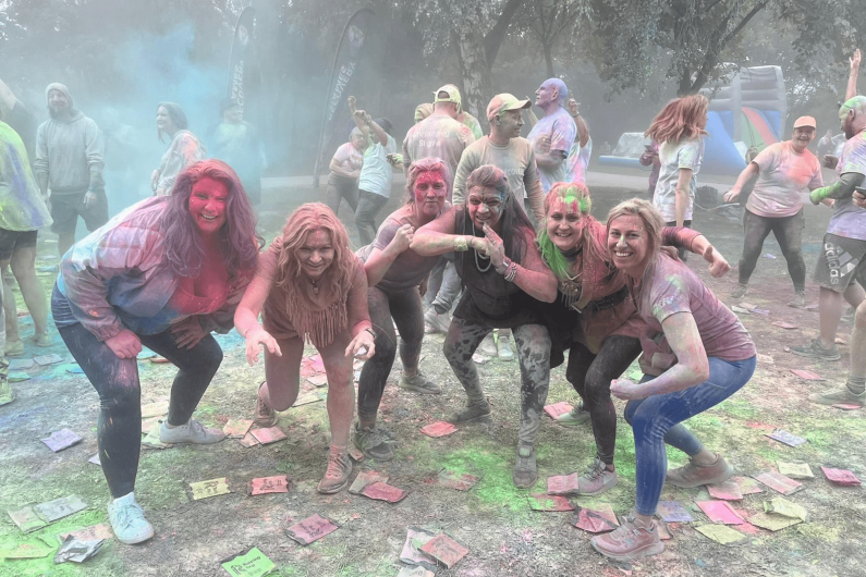 A group of women smiling, covered in and surrounded by colourful powder