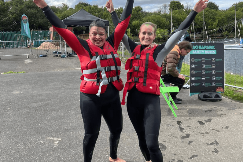 Two women in wetsuits and life jackets smiling