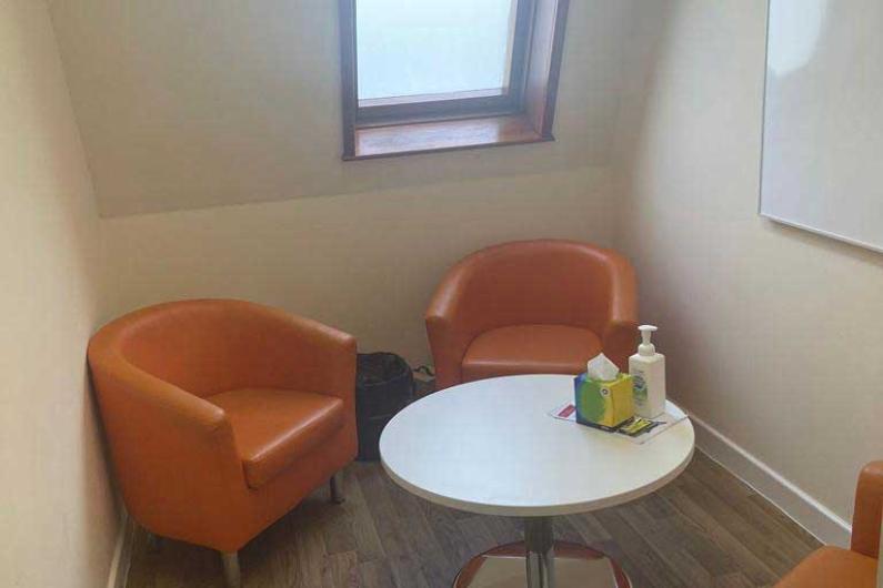 A small room with white walls, three orange tub chairs, a coffee table and a whiteboard