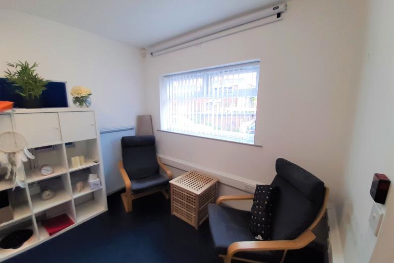 Macclesfield 121 counselling room - a room with a window, white walls, bookshelf and two chairs facing each other