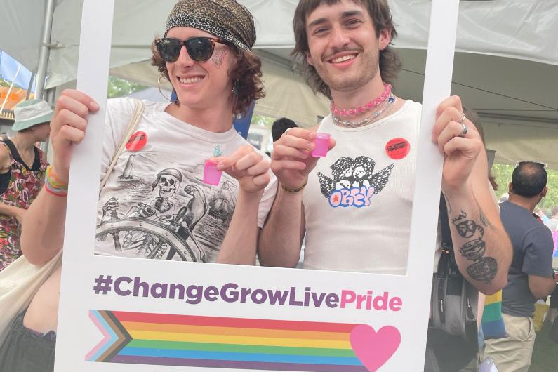 Two people holding up a photo frame with the words #ChangeGrowLivePride on it