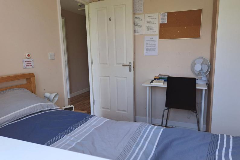 ESH community - bedroom. A blue single bed in a room with white walls, a desk with a black chair and a cork noticeboard