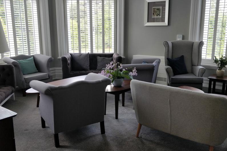 A living room with plush chairs and sofas, with big windows.