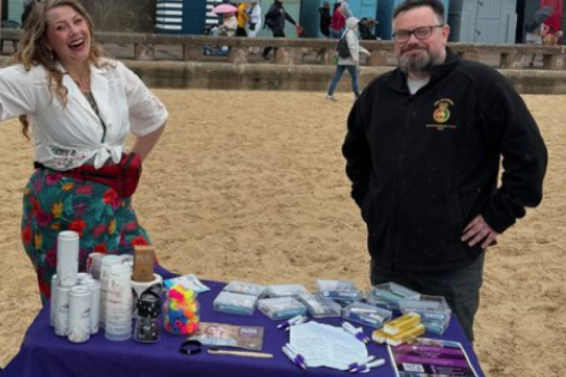 Two people stood on the beach with a table in front of them 