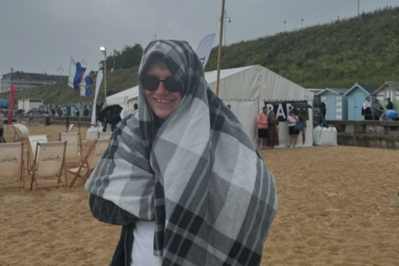 A young man stood on a beach with a blanket wrapped around him