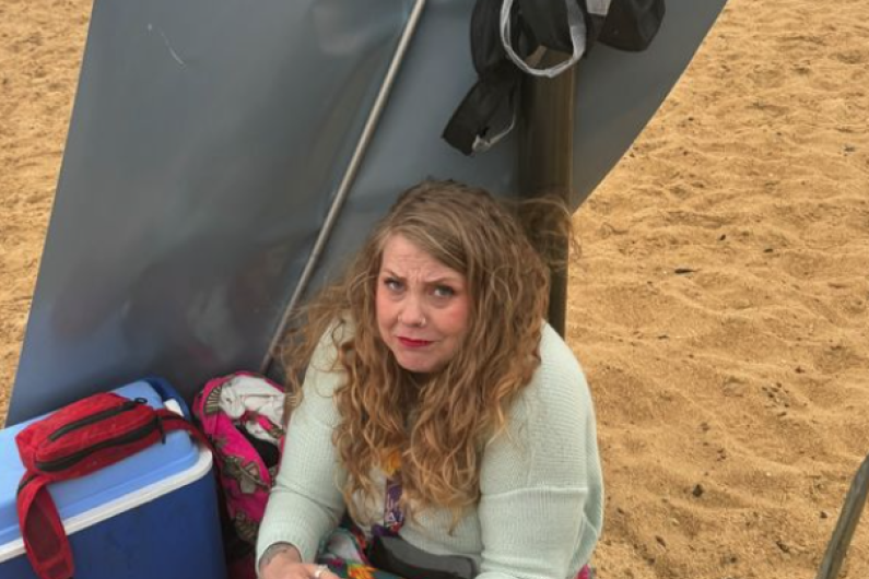 A young woman sand on the beach looking cold.