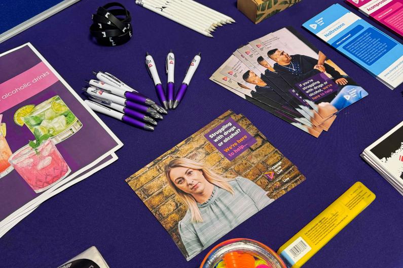 A close up of a table with stickers, leaflets, pens and a naloxone kit on it 