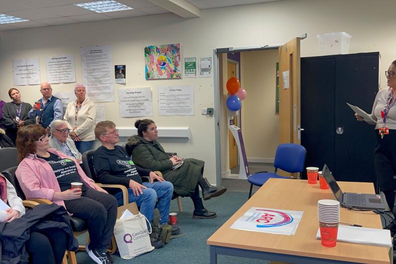 A woman giving a talk to an audience sat in chairs watching her.