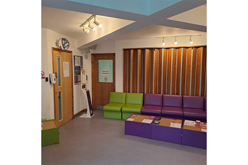 An open room with wooden panelling on one wall and purple sofas in front of it