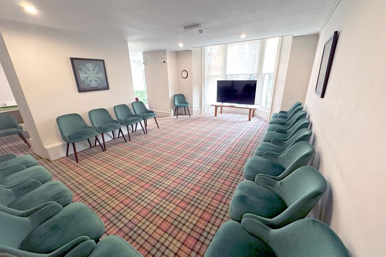 A large room with teal chairs placed around the edge and a TV at the far end